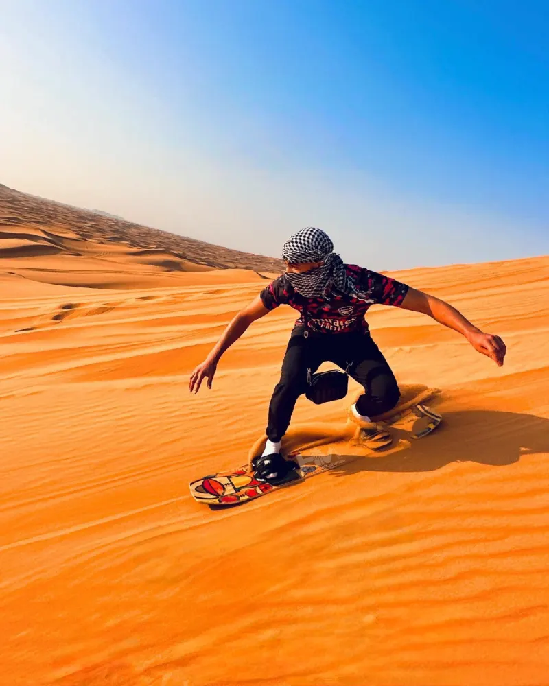 Guest sandboarding down a high red dune near Dubai